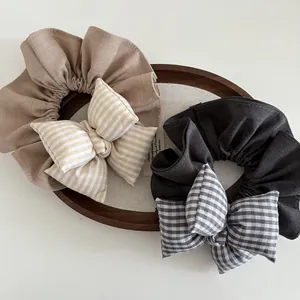 Elastici per capelli con fiocco a quadri e righe in beige e grigio scuro su vassoio di legno