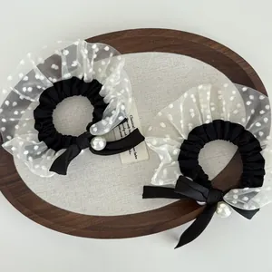 Detail of two black polka dot mesh scrunchies with satin bows and pearl beads in a tray