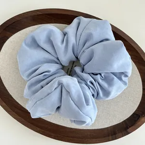 Close-up of a light blue cloud-style fabric scrunchie on a minimalist wooden tray