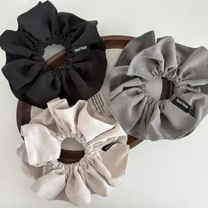 Three oversized matte cotton scrunchies in black, blue, and beige with handmade labels