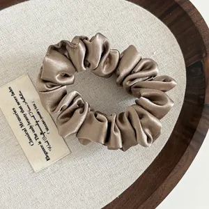 Elastic satin scrunchie in champagne gold with a luxurious glossy finish and soft pleats