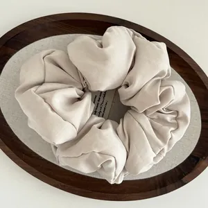 Beige puffy cloud scrunchie in soft matte fabric displayed on a vintage wooden tray