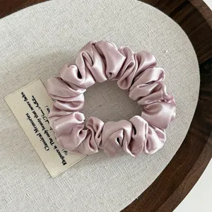 Elegant dusty pink satin scrunchie with silky pleated texture on a wooden tray