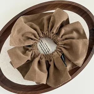 Brown suede scrunchie with visible stitching and woven label in a vintage wooden tray