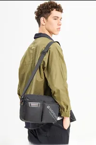 Side view of man wearing a black canvas messenger bag with multi-zippered compartments