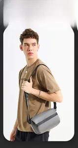 Close-up of a gray waterproof nylon crossbody bag featuring a branded strap on a model