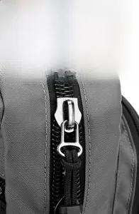 Detail of smooth silver metal zipper with black cord on gray fabric sling bag