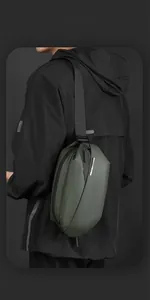 Rear view of a dark green waterproof crossbody bag worn by a model in a black jacket