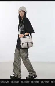Detail of light grey techwear messenger bag with black buckle strap and orange tag