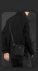 Close-up of black tactical crossbody bag with metal buckle and adjustable strap on a person