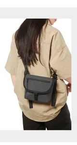 Dark grey nylon crossbody bag with adjustable strap worn by a model in a back view