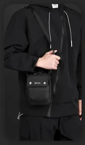Close-up of black crossbody bag with adjustable strap and metallic logo snap button
