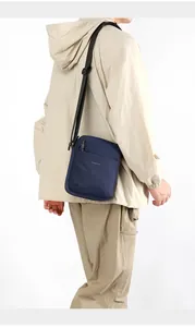 Detail of navy nylon crossbody bag on model showing adjustable strap and zipper pockets