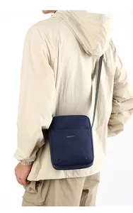 Detailed back view of a dark blue canvas crossbody bag worn with a light trench coat