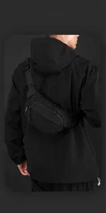 Close-up of black nylon crossbody bag with dual zippers on male model in outdoor setting
