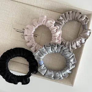 Detail of four colorful pleated satin hair scrunchies with decorative rings in a display tray