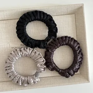 Close-up of three satin scrunchies in black, dark brown, and champagne silver on a tray