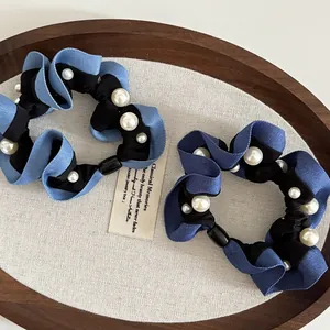 Detail of blue pleated fabric hair scrunchies with white pearls on a rustic wooden tray