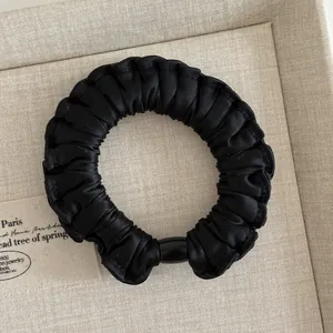 Detail of black ruffled scrunchie with silk texture and decorative polished bead