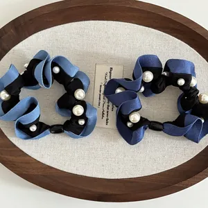 Detailed view of pearl-embellished denim blue fabric scrunchies with pleated texture