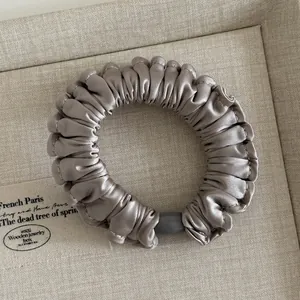 Detailed view of silver satin ruffle hair scrunchie with metallic sheen and elastic band