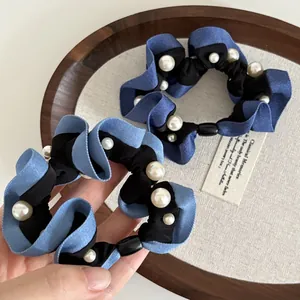 Close-up of denim blue fabric scrunchie featuring white pearls and pleated texture