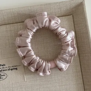 Detail of pink satin ruffled scrunchie showing glossy texture on linen tray