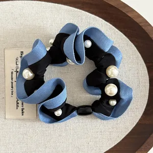 Detail of blue denim fabric hair scrunchie with spiral pearl accents on wooden tray