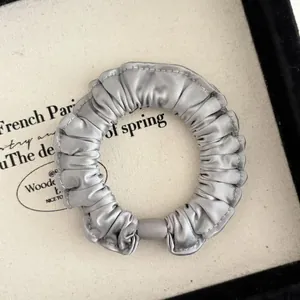 Detailed view of silver satin scrunchie with soft ruffled texture and elegant metal luster