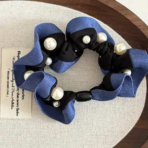 Detail of blue denim fabric hair scrunchie with white pearls on a rustic wooden tray