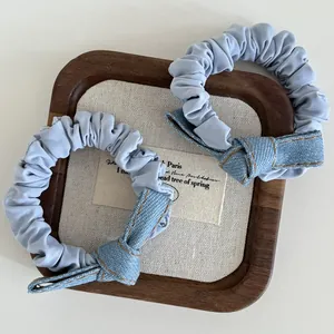 Close-up of light blue denim bow scrunchies with yellow stitching on display tray