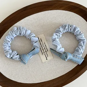 Detail of light blue denim bow scrunchies with yellow contrast stitching on wooden tray