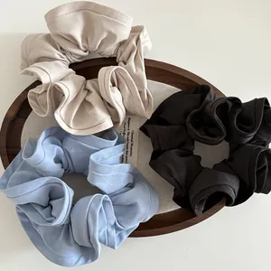 Three large fabric scrunchies in beige, light blue, and black on a wooden tray