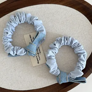 Close-up of light blue scrunchies with denim bow details and yellow stitching accents