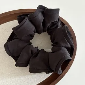 Detail of a black pleated scrunchie with ruffled edges on a wooden tray with linen