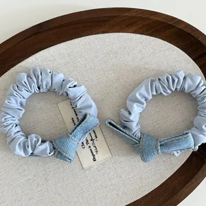 Detail of light blue denim bow scrunchies with yellow stitching on a wooden tray