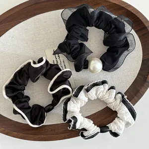 Detail of three black and white scrunchies with mesh lace and pearl decor on a wooden tray