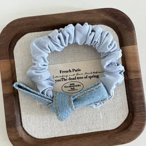 Macro detail of a light blue denim bow scrunchie with yellow stitching on a wooden tray