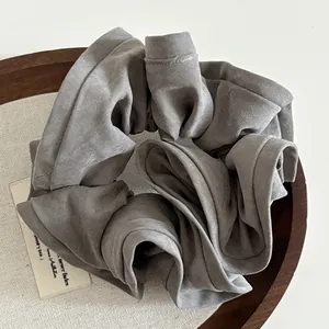 Detailed view of a dark grey ruffled fabric scrunchie on a wooden tray with soft lighting