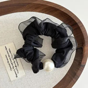 Close-up of a black mesh scrunchie featuring a large faux pearl on a wooden tray