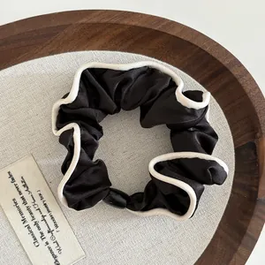 Close-up of black satin scrunchie with cream lace edge on a rustic wooden tray