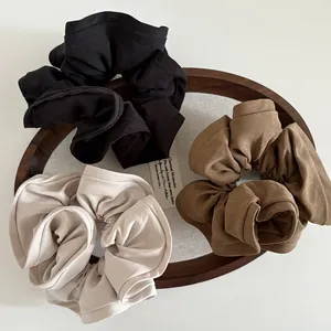 Three oversized fabric scrunchies in black, brown, and cream white displayed on a wooden tray