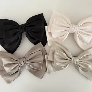 Flat lay of satin bow hair clips in black, cream white, champagne gold, and silver grey