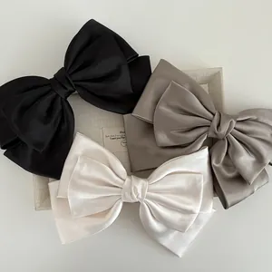 Close-up of three layered satin bow hair clips in black, beige, and champagne colors