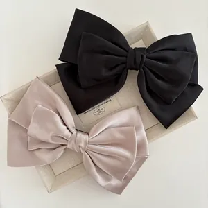 Detailed close-up of premium champagne and black satin bow hair clips on a fabric tray