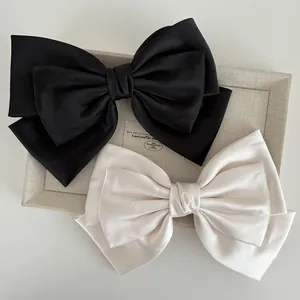 Detailed view of layered satin bow hair clips in black and cream with silky finish