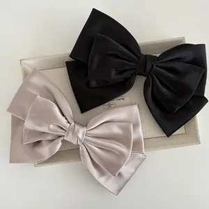 Detail of satin bow hair clips in black and champagne on a beige display tray
