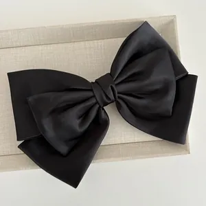 Detail of multi-layered large black satin bow clip on a beige linen display tray