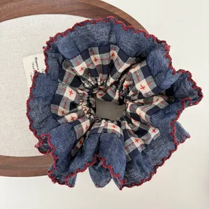 Detail of navy denim and plaid scrunchie with red cross-stitch and scalloped edges
