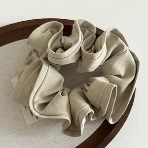 Elegant beige fabric scrunchie with ruffled edges displayed on a rustic wooden tray